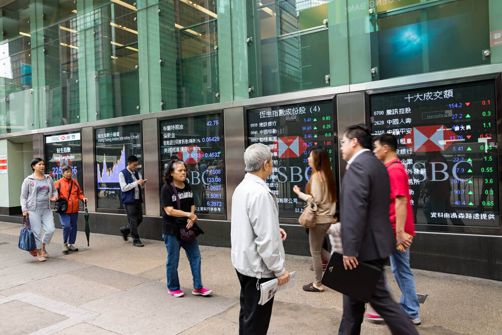 Asian shares are shown on electronic boards as people are walking by